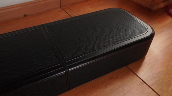 The soundbar itself is wide but low-profile, designed to sit neatly under modern TVs without blocking the screen